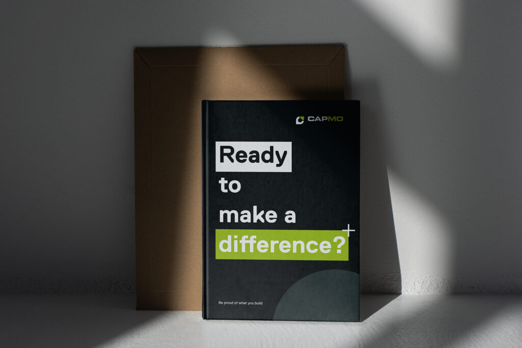 Schwarzes Capmo Notizbuch mit der Aufschrift "Ready to make a difference?" lehnt an weißer Wand