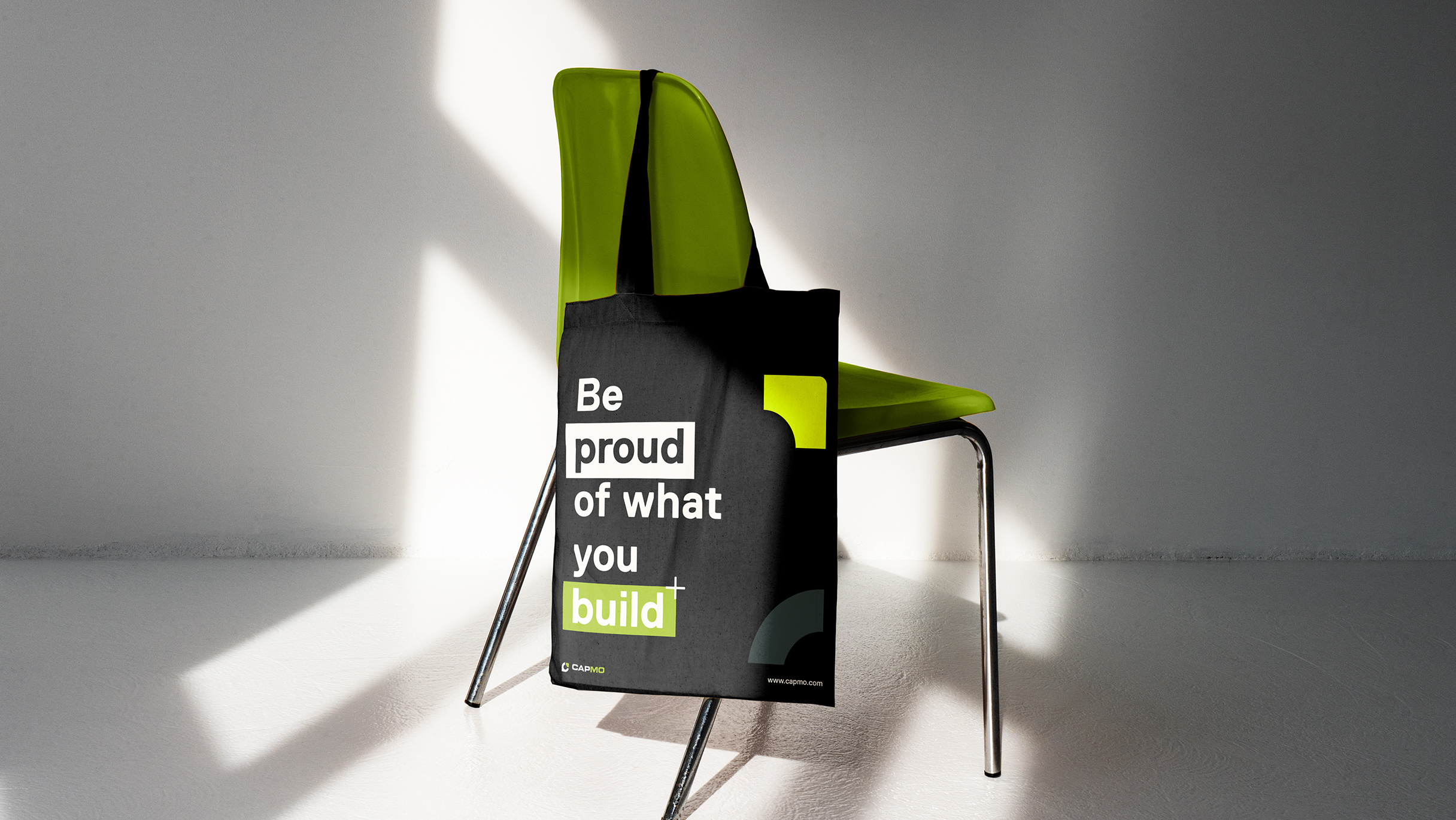 Über einem grünen Stuhl hängt ein schwarzer Jutebeutel mit der Aufschrift: Be proud of what you build.